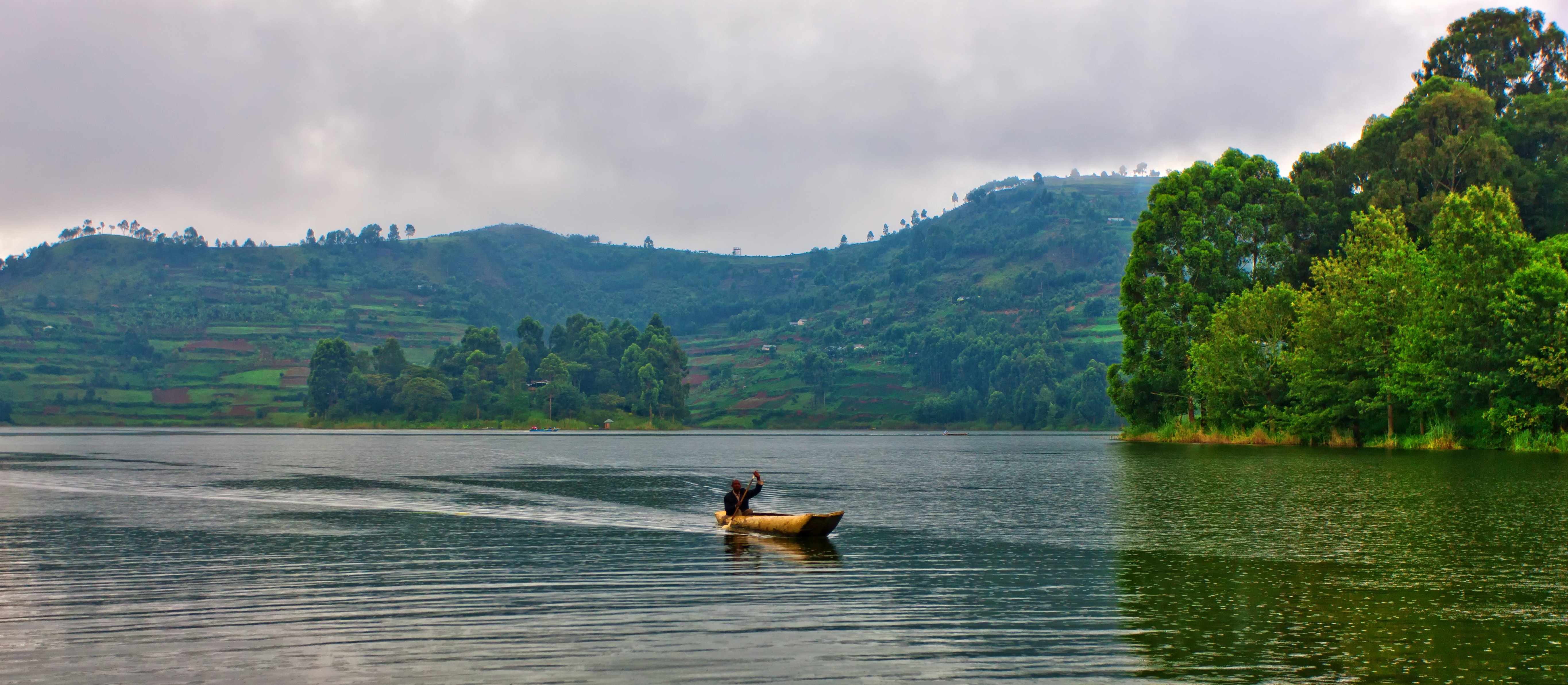 Wooden canoe crossing the calm waters of Lake Bunyonyi, surrounded by green hills in southwestern Uganda.