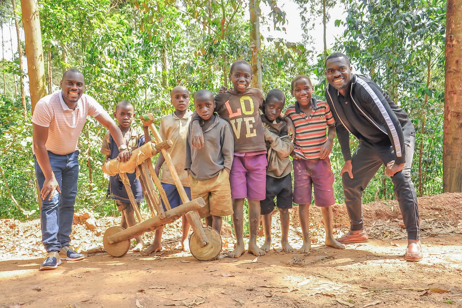 Village boys riding a handmade wooden bicycle in rural Uganda.