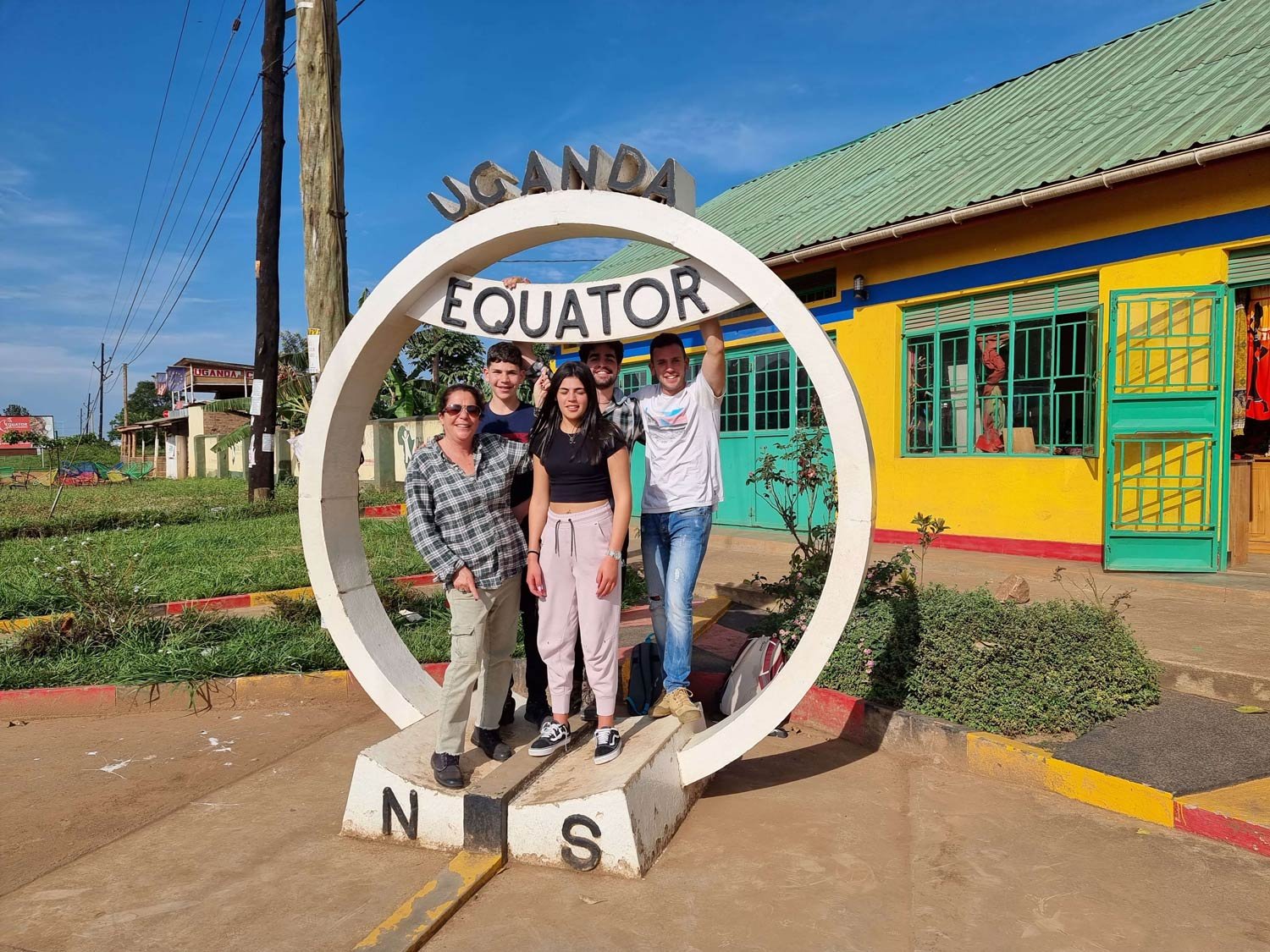 Image 8: Uganda Safari- Four people stand under a circular equator sign marked 