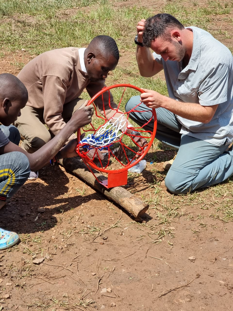 A team member at Amatsiko's community school adjusts a basketball hoop outside a brick classroom building, one small example of how tourism revenue funds real infrastructure in Kabale