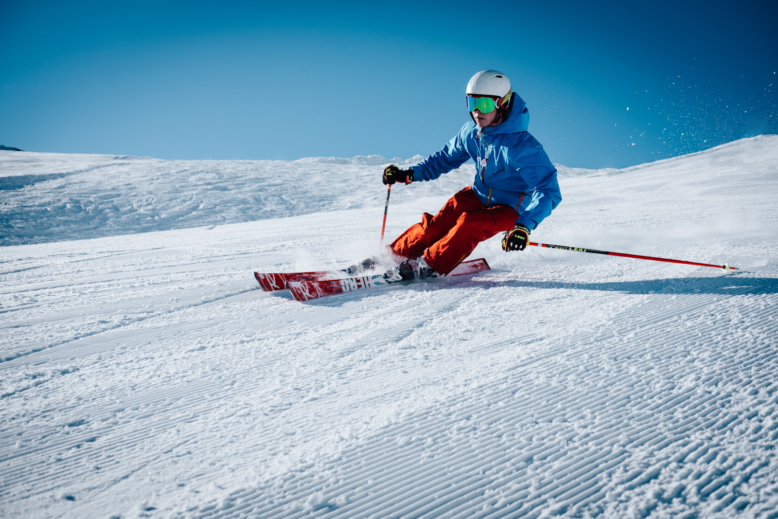 A skier in a blue jacket and red pants carves a clean turn on a snowy slope in crisp winter light