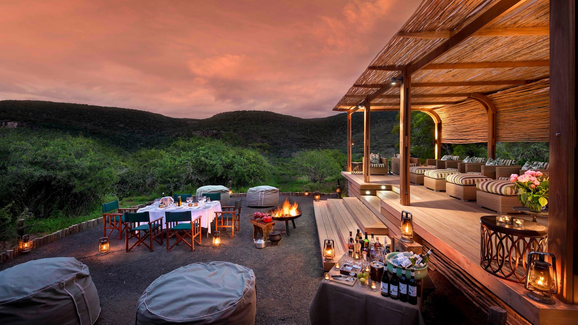 An outdoor dinner setup at a safari lodge, fire crackling as the sun drops, the kind of evening that follows a long day on the savanna
